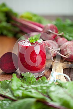 Glass of fresh beetroot juice with bets on wooden table.