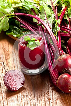 Glass of fresh beetroot juice with bets on wooden table.