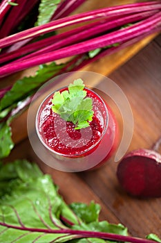 Glass of fresh beetroot juice with bets on wooden table.