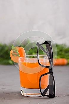 A glass of fresh carrot juice and black-rimmed spectacles