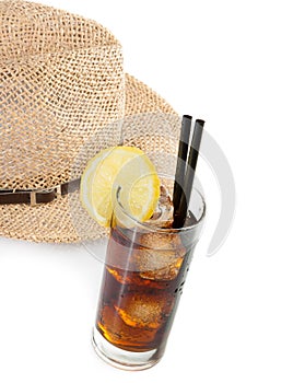 Glass of fresh coke with straw in front of summer hat, summer time