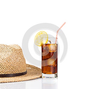 Glass of fresh coke with straw near summer hat, summer time