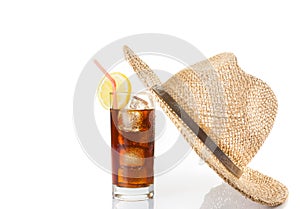 Glass of fresh coke with straw near summer hat on top, summer time