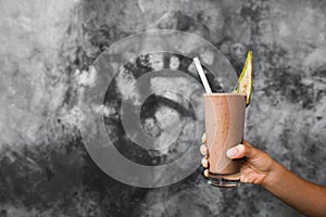 Glass of fresh cold chocolate milk shake in woman hands on gray background