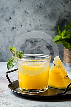 Glass of fresh golden watermelon juice or smoothie with slices of watermelon. Refreshing cold summer fruit drink.