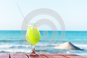 A glass of fresh green tropical fruit juice on the beach, on the table, against the sea