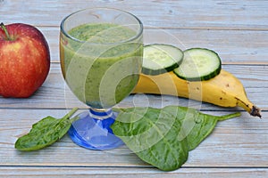 Glass of fresh healthy green smoothie, a red apple, banana, cucumber, and spinach