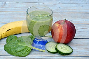 Glass of fresh healthy green smoothie, a red apple, banana, cucumber, and spinach