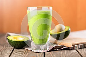 Glass of fresh juice and avocado halves on wooden