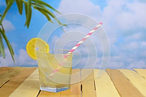 A glass of fresh lemonade on ice with a lemon garnish and a fun red and white barber pole style straw on a rustic wooden table