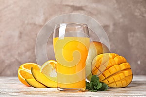 Glass with fresh mango juice and tasty fruits on table