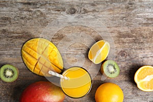 Glass with fresh mango juice and tasty fruits on wooden table, flat lay