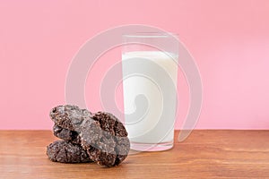 Glass of fresh milk with crunchy baked chocolate sugar cookies on wooden table with pink background