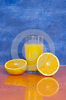 Glass of fresh orange juice with fresh fruits on blue background