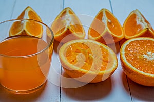 A glass of fresh orange juice with sliced oranges on a wooden table. Preparation of fresh orange juice