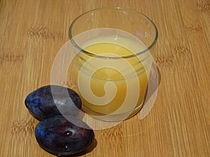 A glass of fresh orange juice and two plums.