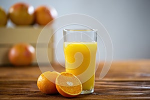 Glass of fresh orange juice on wooden table with grapefruits in background