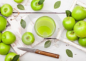 Glass of fresh organic apple juice with granny smith green apples in box on wooden background with knife