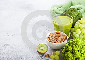 Glass of fresh smoothie juice organic green toned fruit and vegetables on stone kitchen background. With almond nuts in bowl.