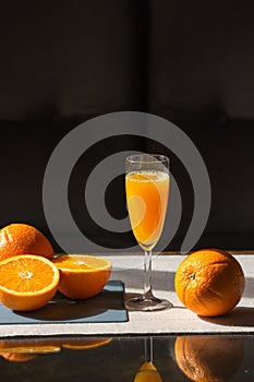 Glass of fresh squeezed orange juice with raw oranges on cutting board isolated on black background. Healthy eating.