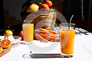 Glass of fresh squeezed orange juice on the table of the kitchen. Ripe bio citrus fuits and vegetables in background.