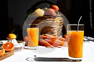 Glass of fresh squeezed orange juice on the table of the kitchen. Ripe bio citrus fuits and vegetables in background.