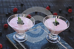 Glass of fresh strawberry and blueberry milkshake smoothie and fresh strawberries on pink black and wooden background