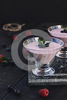 Glass of fresh strawberry and blueberry milkshake smoothie and fresh strawberries on pink black and wooden background