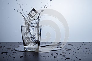 Glass of fresh water with splash and ice on dark table and blue background