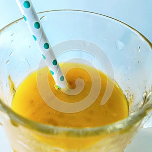 A glass of fresh yellow smoothie with a straw. Summer and tropical smoothies. Cold blended drinks, fruit smoothie.