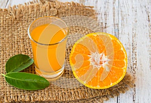 Glass of freshly pressed orange juice with sliced orange on wood