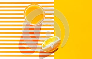 Glass of freshly squeezed orange juice with pulp fruit wedge on duotone bright sunny yellow and white striped background