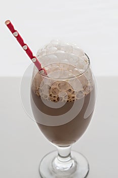 Glass of frothy chocolate milk with red paper straw photo