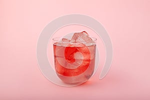 Glass of fruit ice tea. Red iced drink with fruit flavor on pink background. Refreshing lemonade with ice cubes