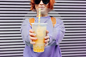 Glass of fruity sugar flavored tapioca pearl bubble tea with straw in hand of hipster fashion woman in sunglasses and