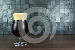 Glass full of Belgian beer on wooden table and stone background