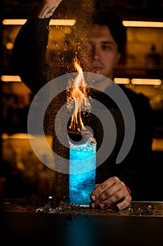 glass full of ice and drink with fire and hand of bartender accurate sprinkle powder on it