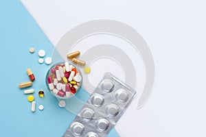 A glass full of pills, tablets, capsules on blue and white background, with empty space for text. Top view