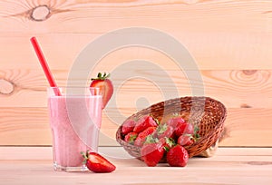 A glass full of strawberry drink and a box with berries on a wooden background. Strawberries in a basket and a glass of yogurt.