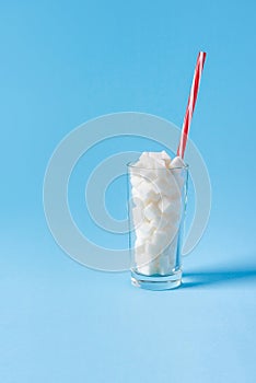 Glass full of sugar cubes with straw isolated on blue background. Unhealthy diet concept. Copy space