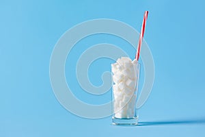Glass full of sugar cubes with straw isolated on blue background. Unhealthy diet concept. Copy space