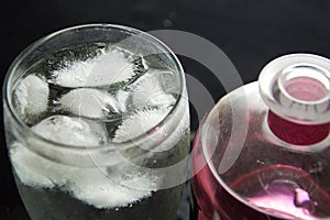 Glass with gin and tonic with a lot of ice and bottle of pink gin