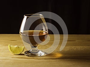 Glass glass with cognac on a wooden table, lemon slice, dark background. Free space for text on the side