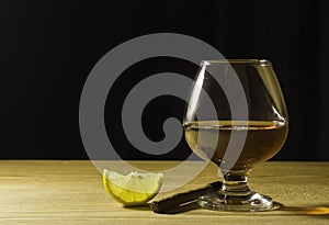 A glass glass of cognac on a wooden table, a slice of lemon and a cigar Free space for text on the side