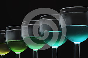 glass glasses with a green cocktail or wine in a row on a black background