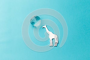 A glass globe and a giraffe figure on a light blue background. The concept of protecting wild animals in Africa