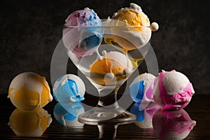 Glass goblet with multi-colored ice cream balls on a black background with balls on the table. AI generated