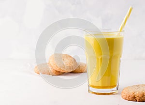 A glass of golden milk on a white background next to cookies. Traditional healthy indian drink.