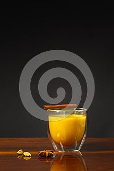 A glass of golden moon milk with turmeric and a stick of cinnamon. Hot drink with spices. Close-up, vertically with space