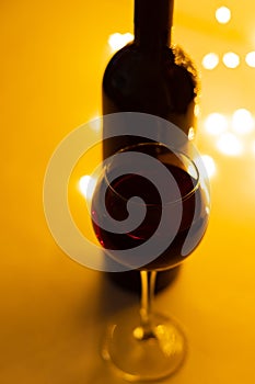 A glass of good red wine, a close-up, a bottle and a bokeh of lights.